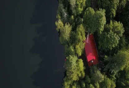 Top down aerial view of a cottage on a lake surrounded by dense forest
